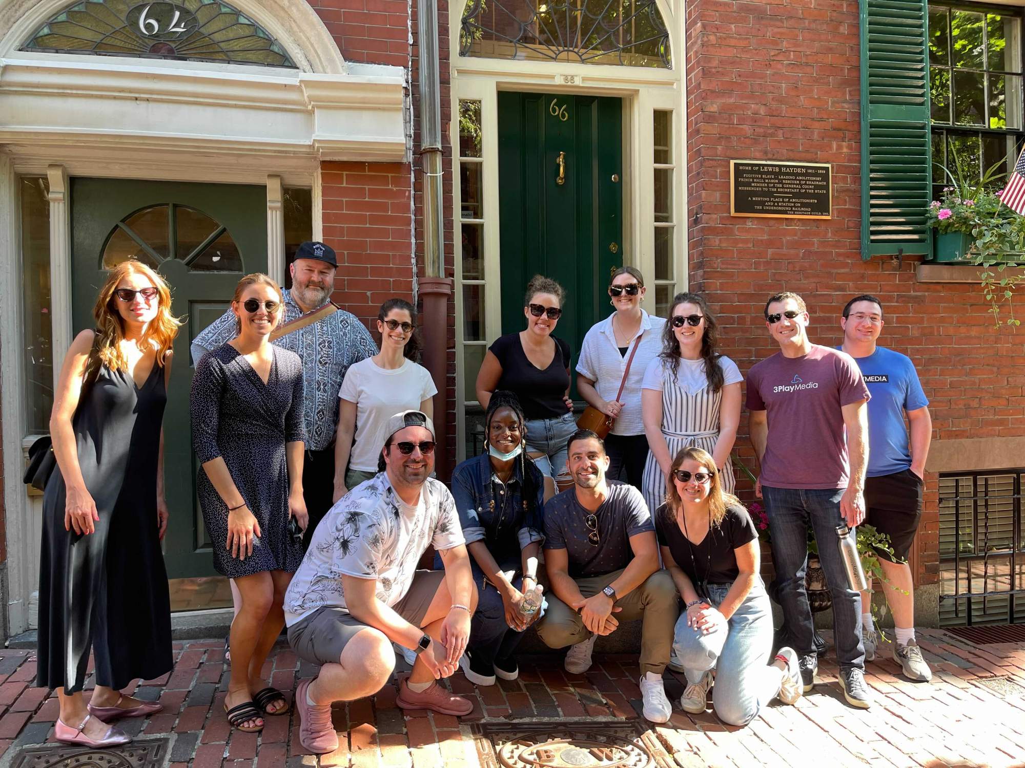 Employees pose gathered smiling in a group, in front of a historic brick building in Beacon Hill. 