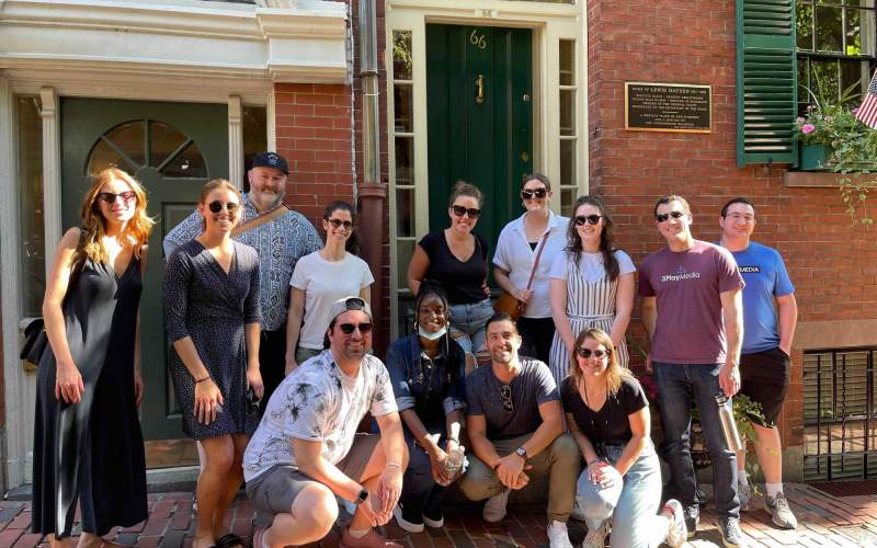 Employees pose gathered smiling in a group, in front of a historic brick building in Beacon Hill. 